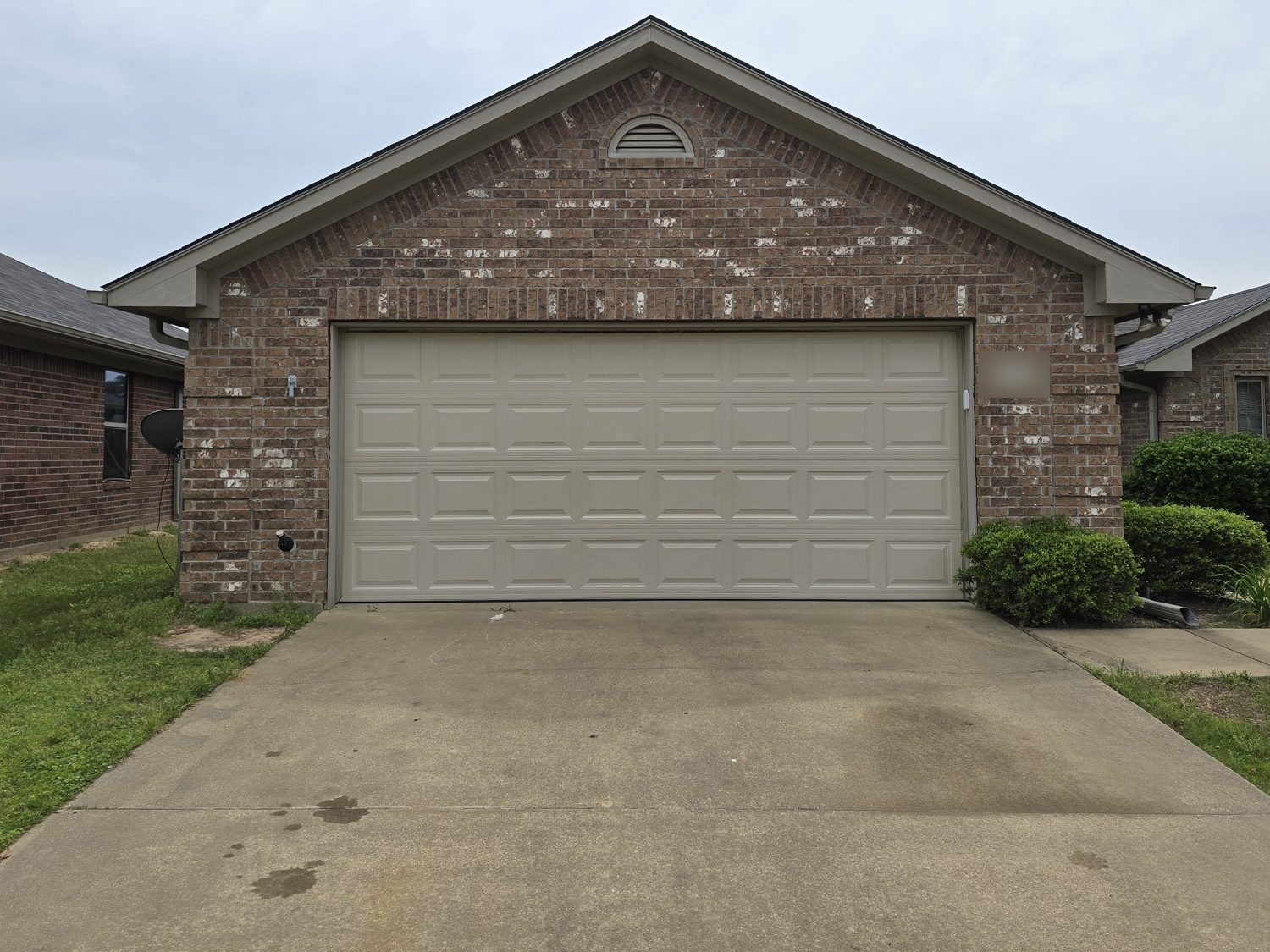 After: the same brick house with a new tan raised-panel garage door