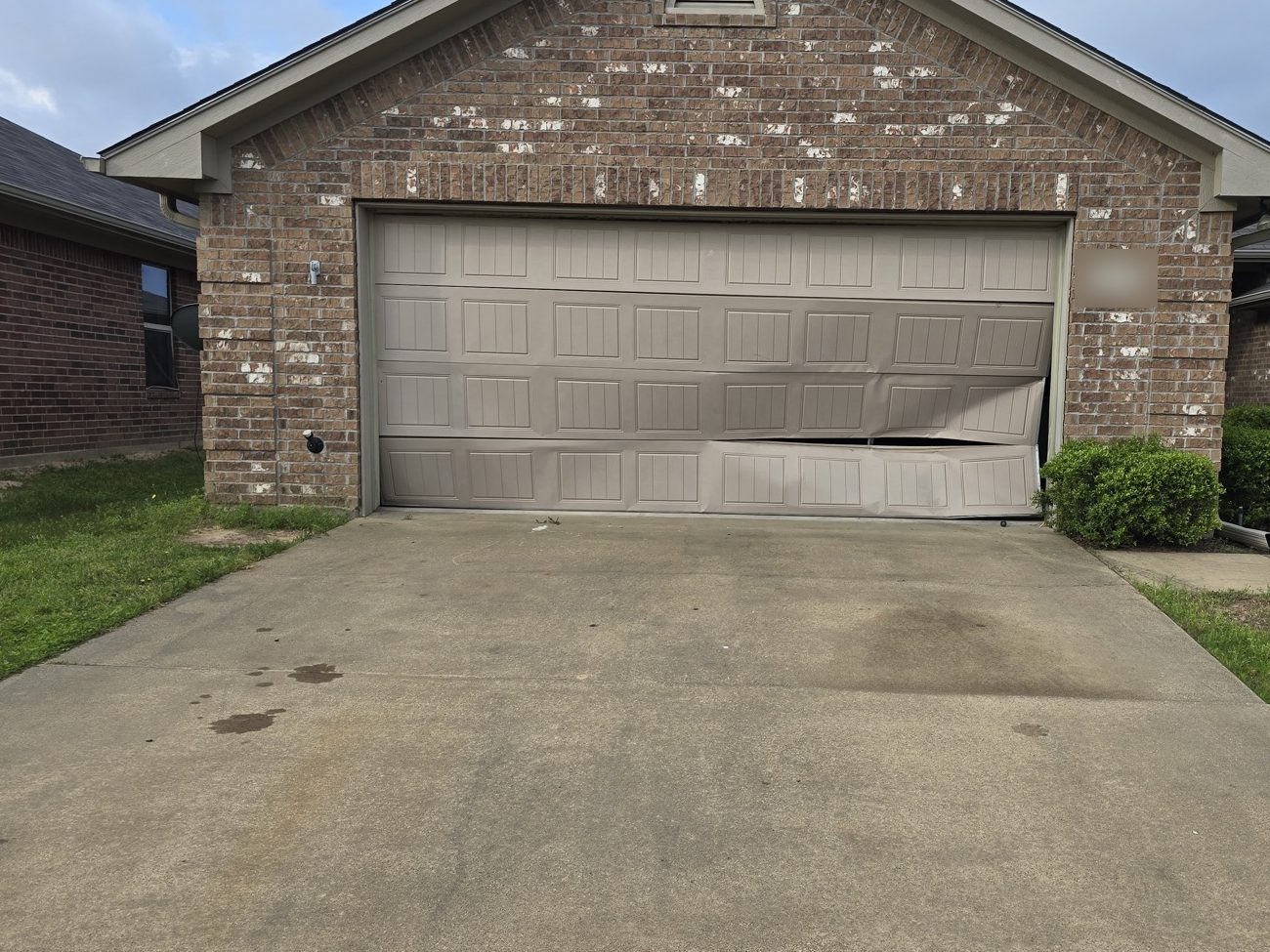 Before: a garage door on a brick house, bent and pushed off its track