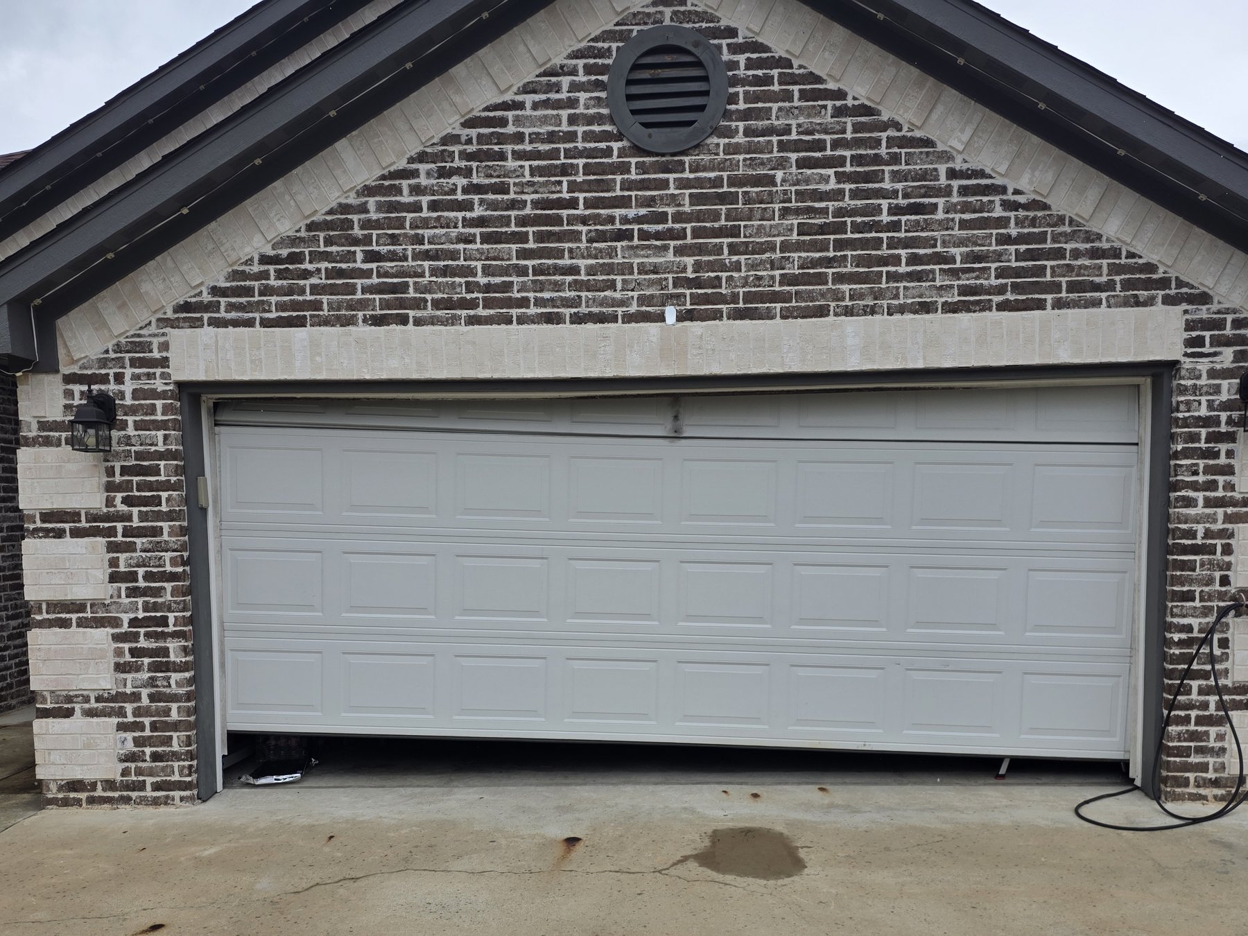 Before: a white garage door hanging crooked and off its track on a brick house